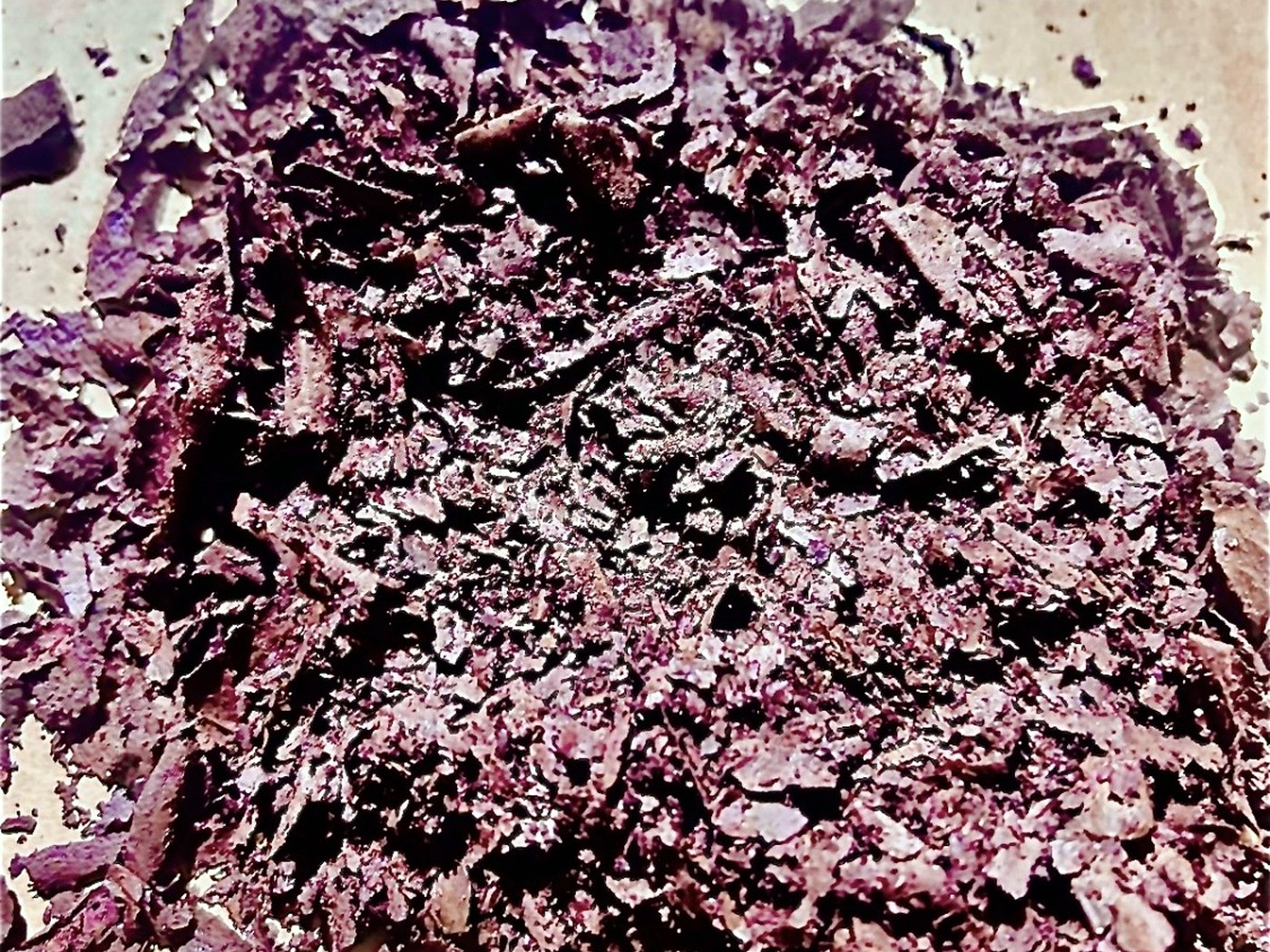 A mound of coarse purple-brown mineral flake concentrate spread on paper for particle size inspection