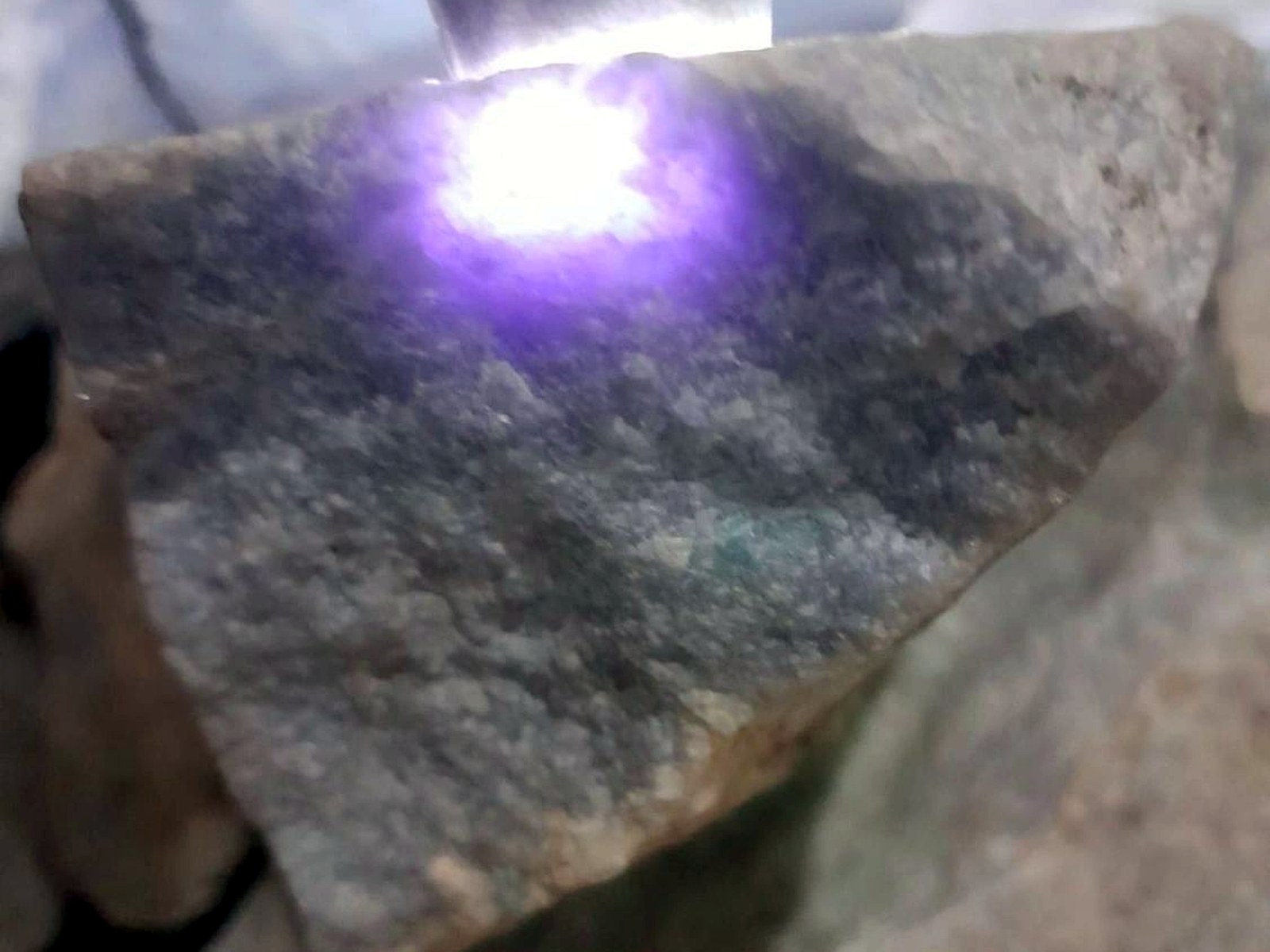 A bright violet laser spot burning a test point on a grey rock sample during spectrometry analysis
