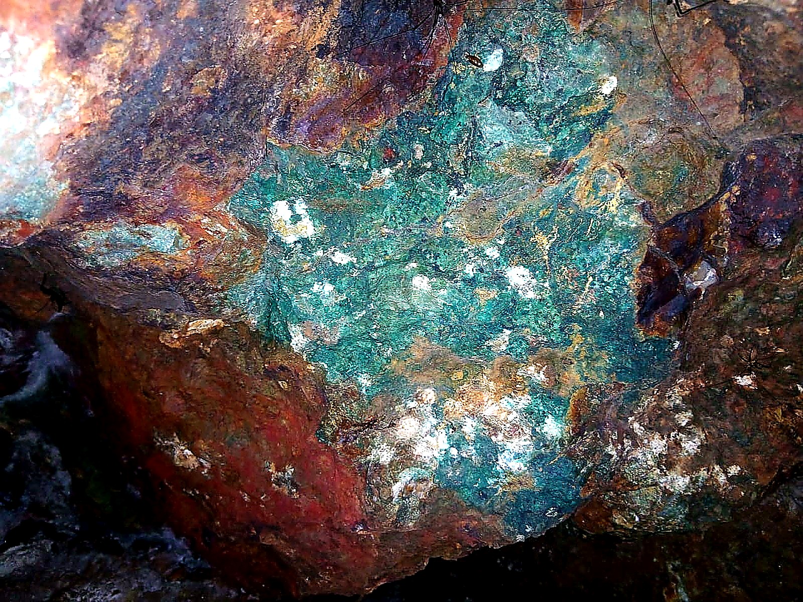 Rock face underground with a large patch of bright green copper carbonate staining surrounded by rust-red oxidised rock