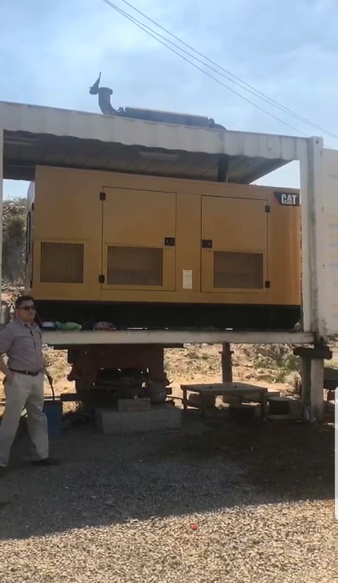 Large yellow CAT generator installed inside an open-sided white shipping container at a mine site
