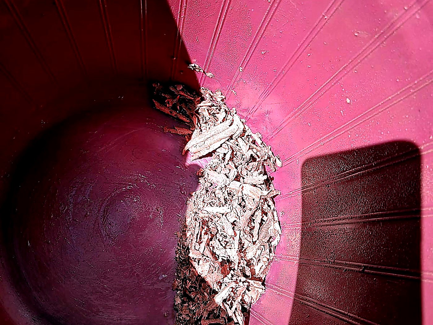 Bright metallic copper flake collected against the wall of a purple plastic collection drum