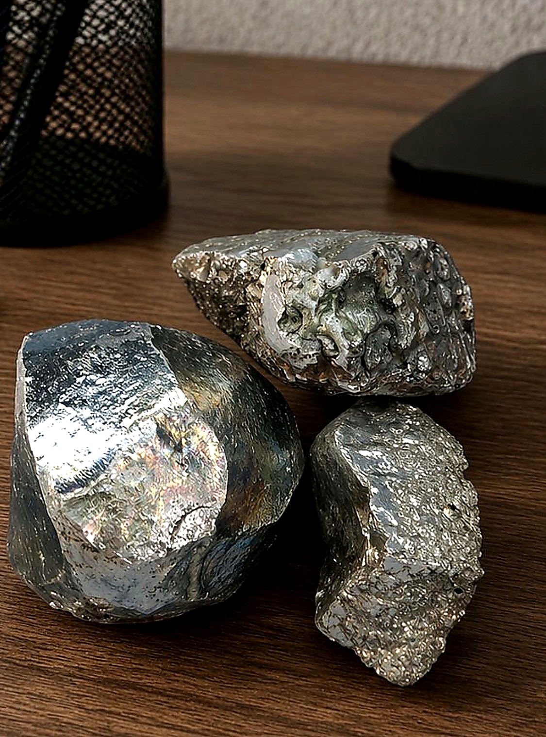 Three bright silvery metallic platinum and nickel bearing mineral specimens on a wooden desk