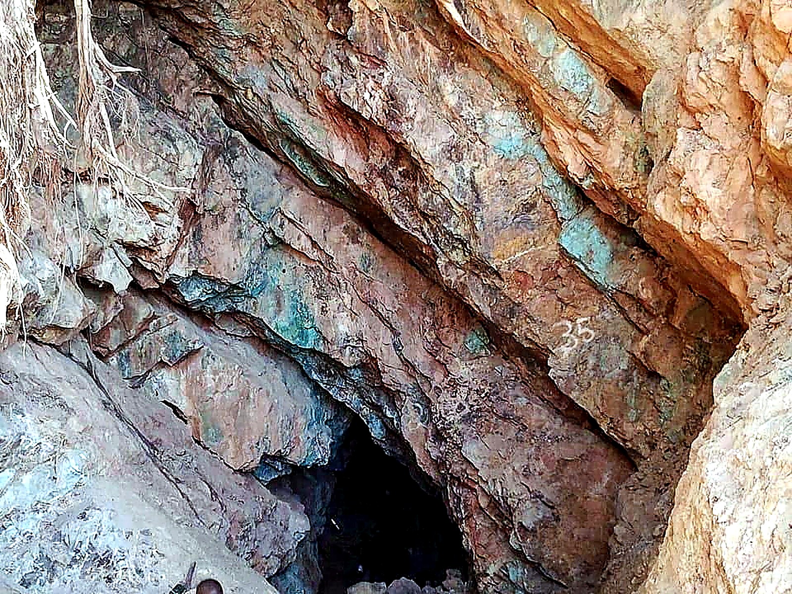 A dark underground adit portal cut into rock covered in turquoise copper oxidation staining