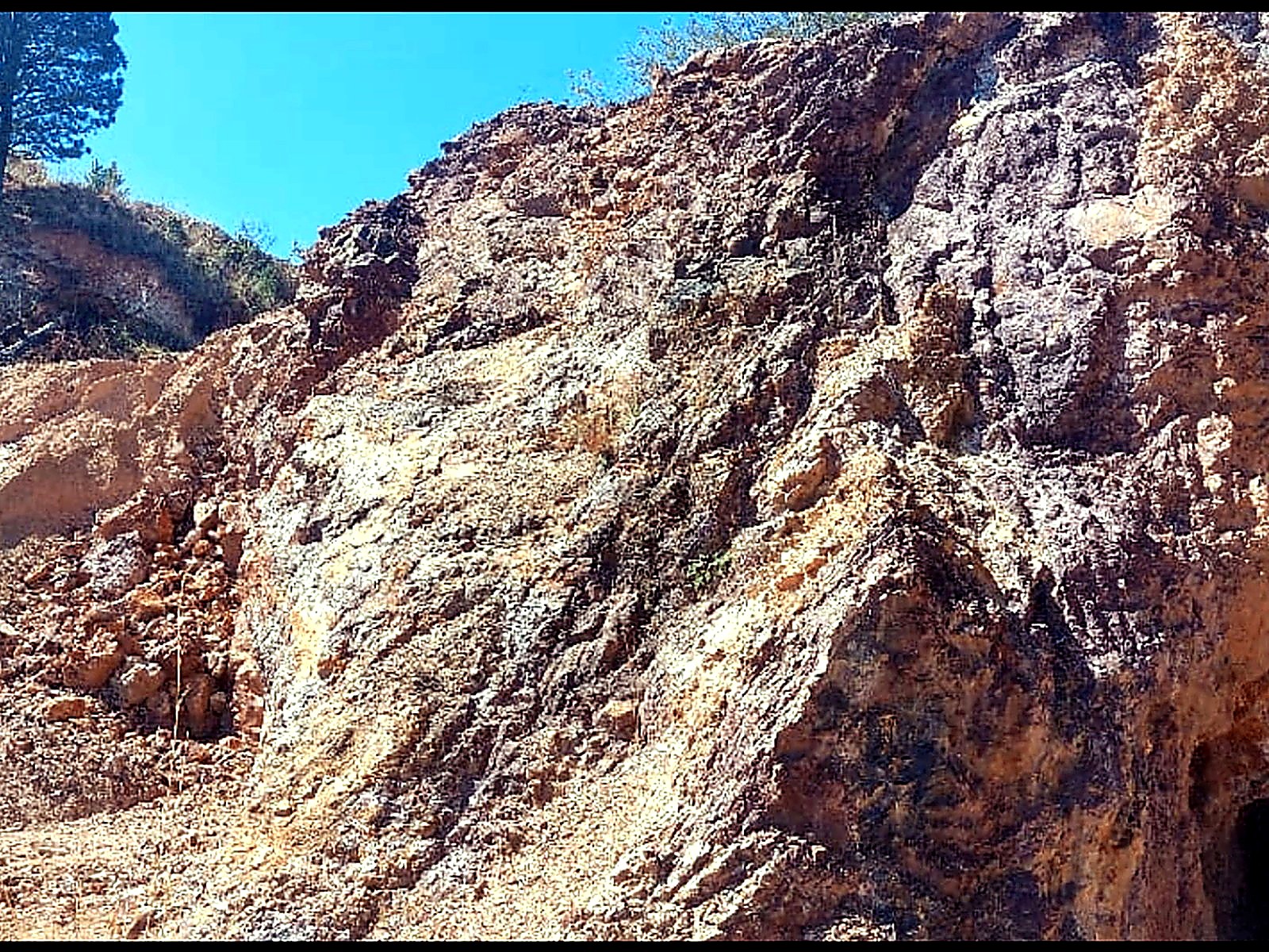 Steep tan and orange rock face on a hillside with a dark tunnel entrance at its base