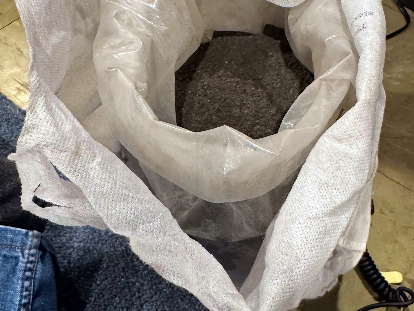 A sealed white sample bag of grey mineral concentrate prepared for independent laboratory assay