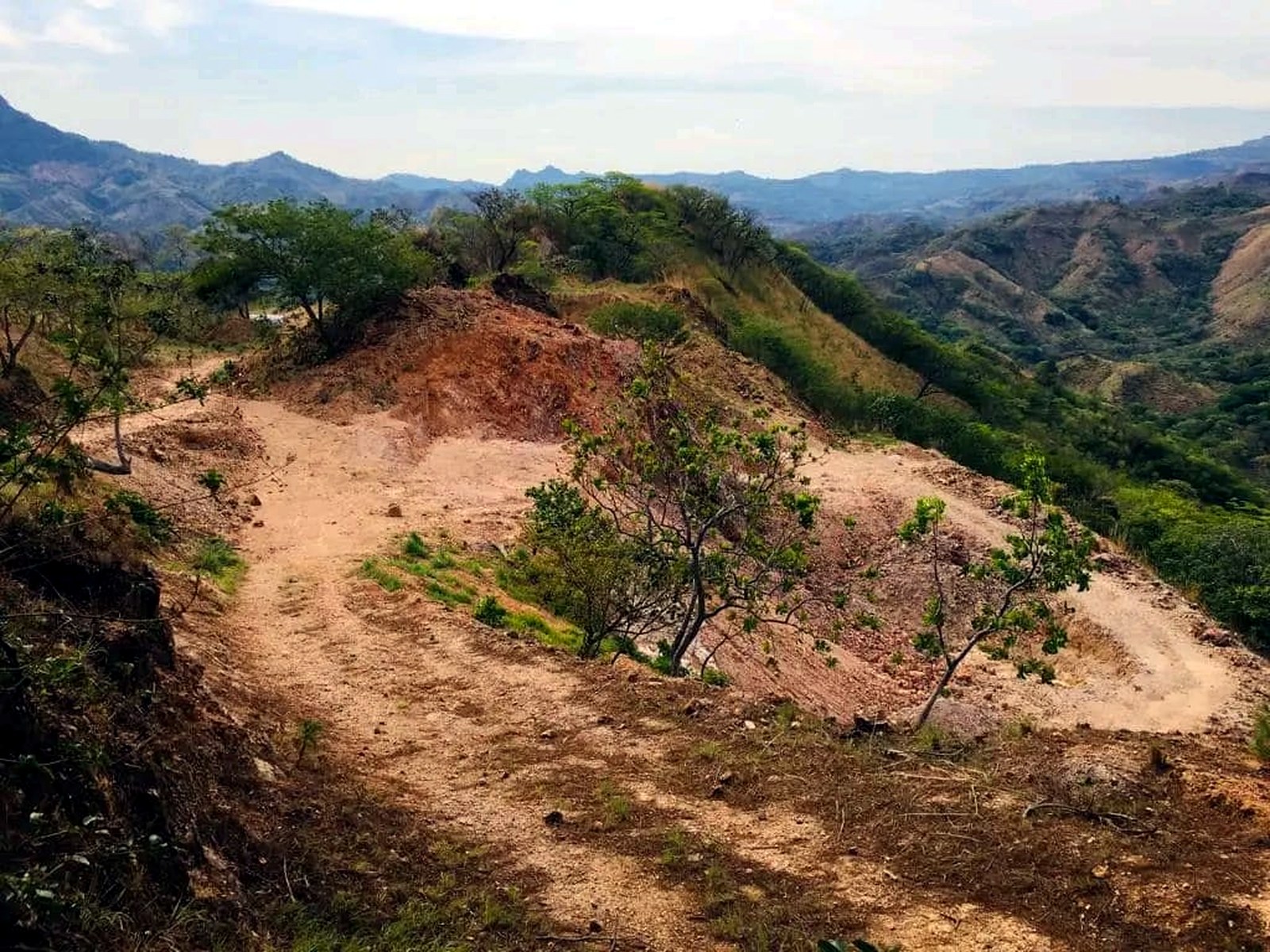 Dirt access track cut along a forested ridge line with green Honduran valleys and mountains behind it