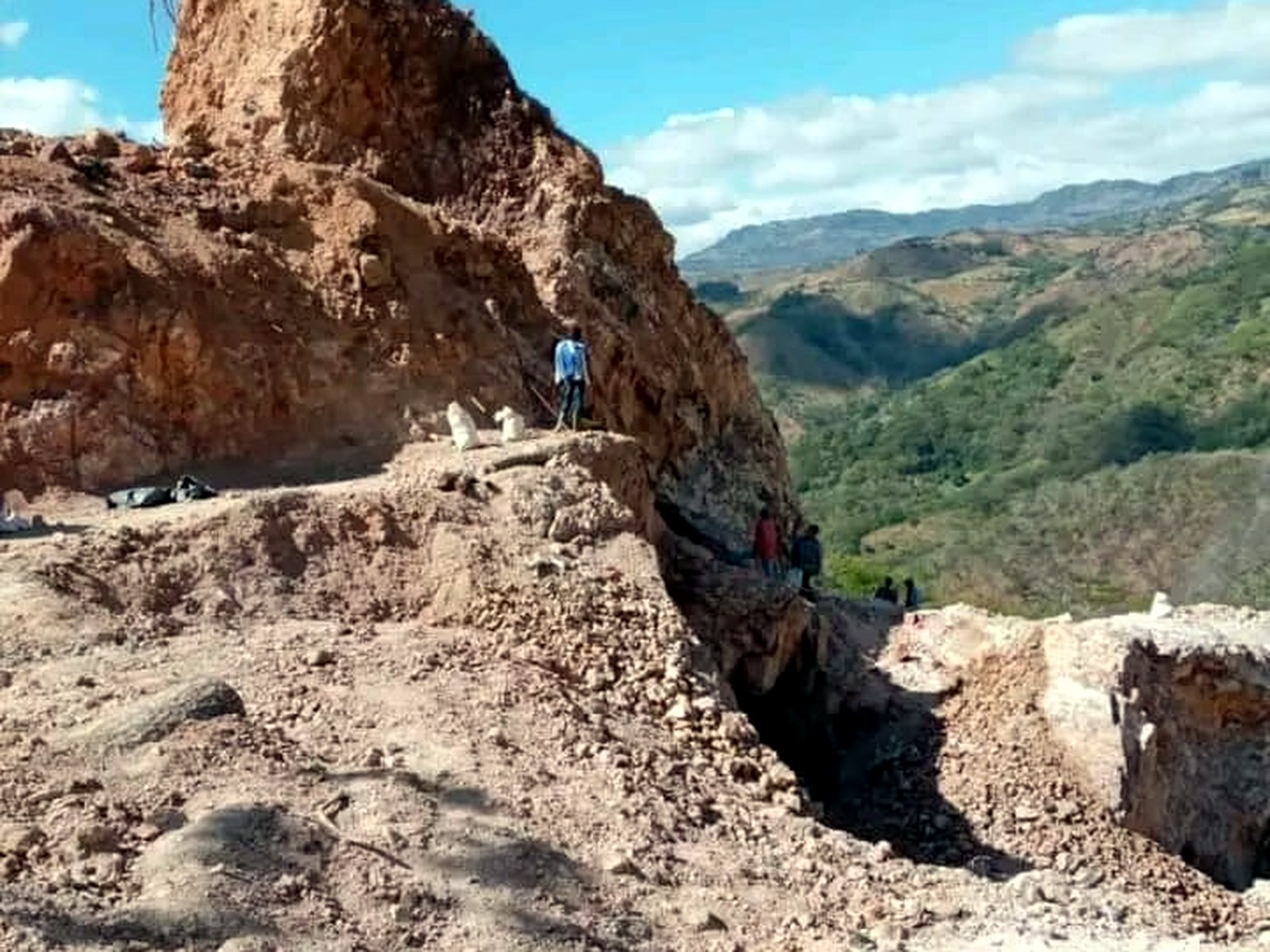 Steep rock face of orange, purple and white oxidised mineralised rock under blue sky at a Honduran concession