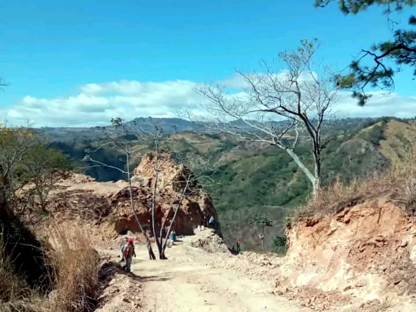Graded dirt mine road running along a Honduran hillside with several workers walking toward the working face