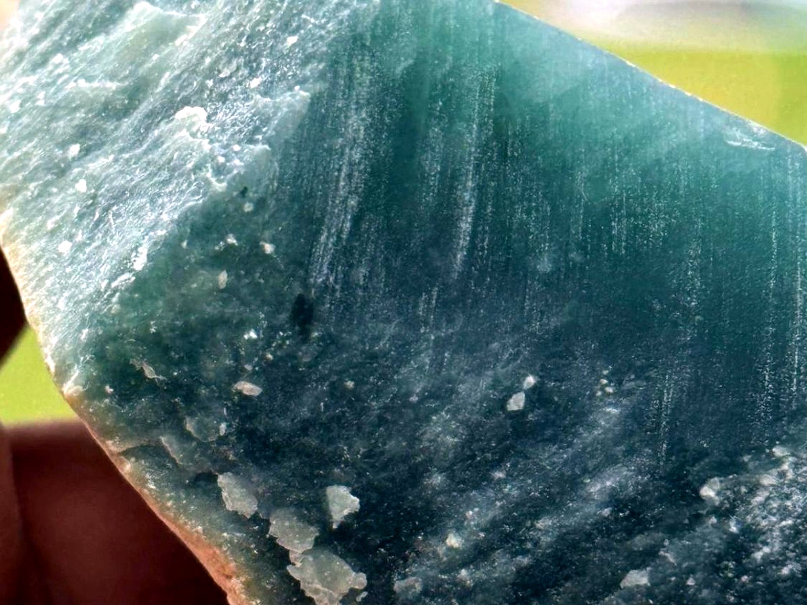 A hand holding a large block of blue-green jade rough with a fine banded texture