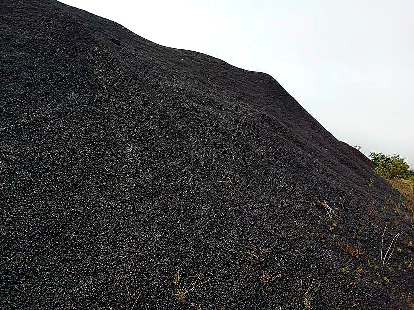A large sloping stockpile of dark grey-black magnetite iron ore fines under an overcast sky