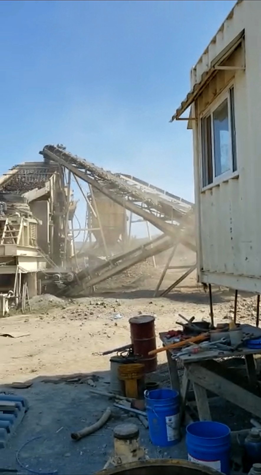 White site office cabin in the foreground with an operating crushing plant and conveyors behind