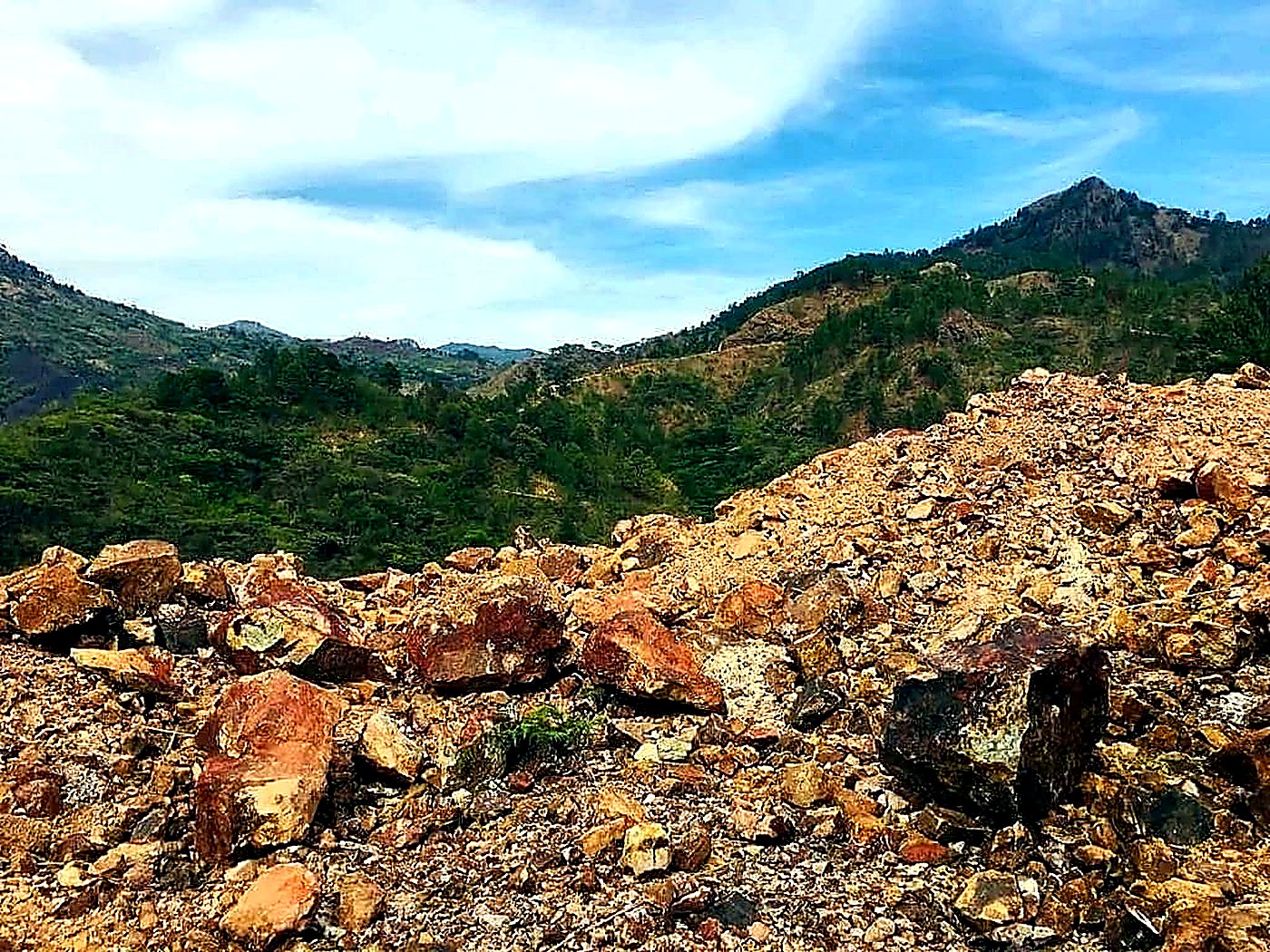 A large stockpile of reddish-brown run-of-mine iron ore rock beneath a cloudy sky