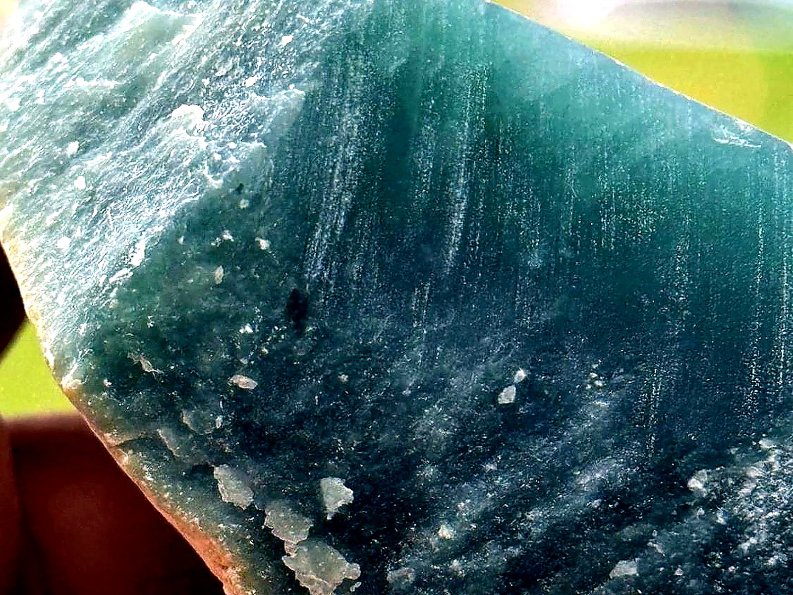 A hand holding a large block of blue-green jade rough with a fine banded texture
