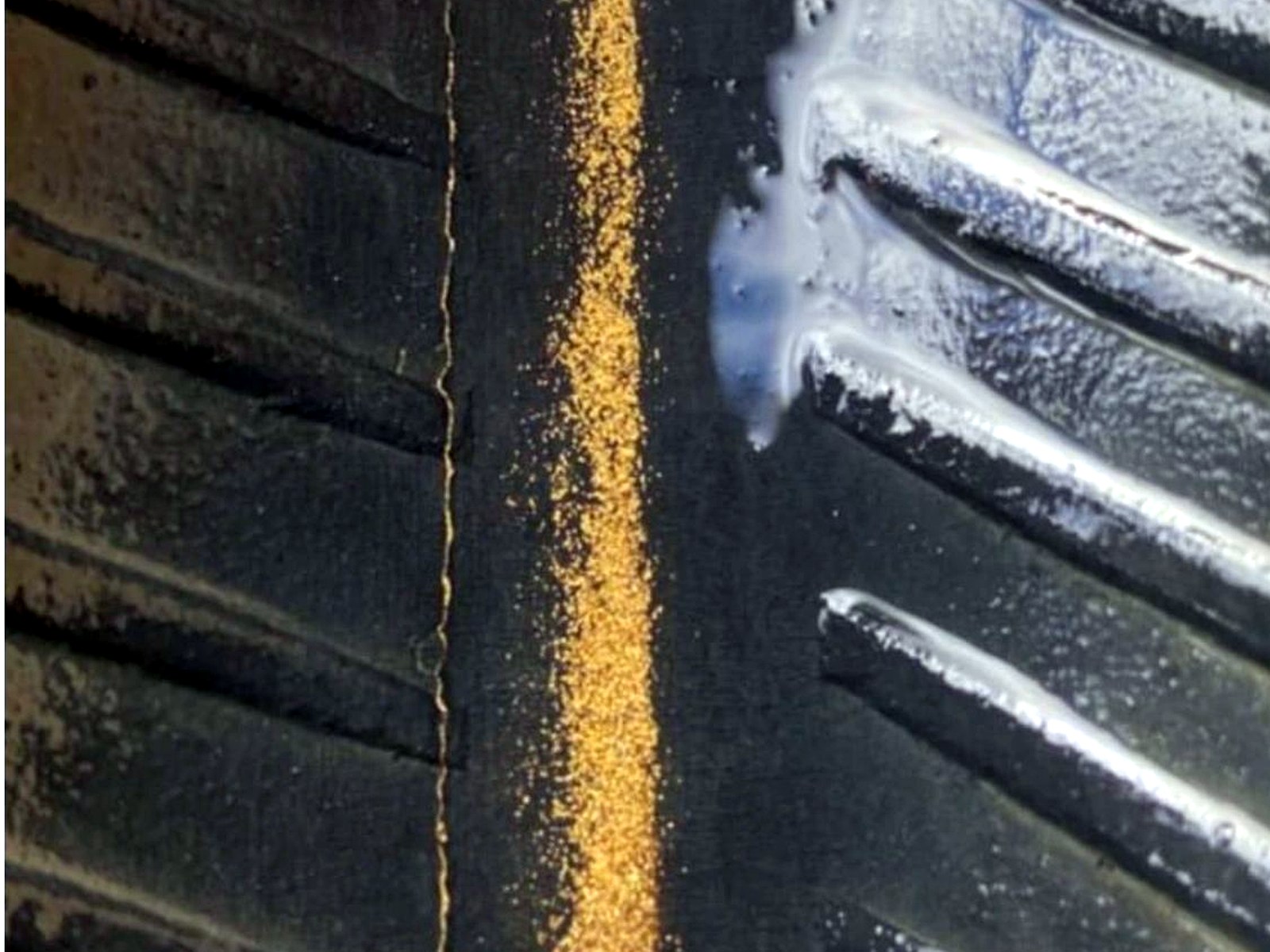 A line of bright yellow gold particles trapped along the black rubber riffles of a wash plant sluice mat