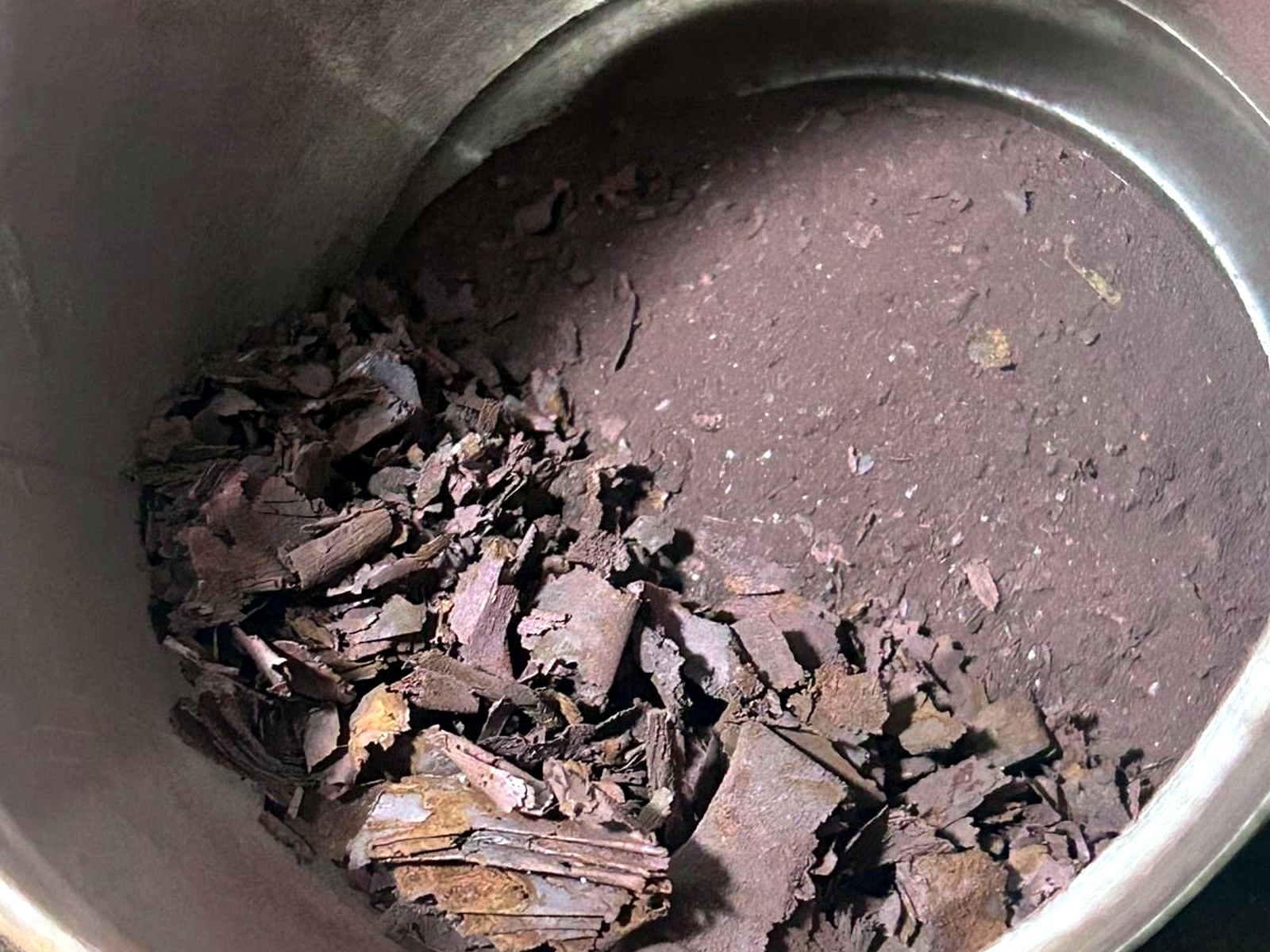 Dark purple-brown coarse mineral flake concentrate collected inside a steel drum