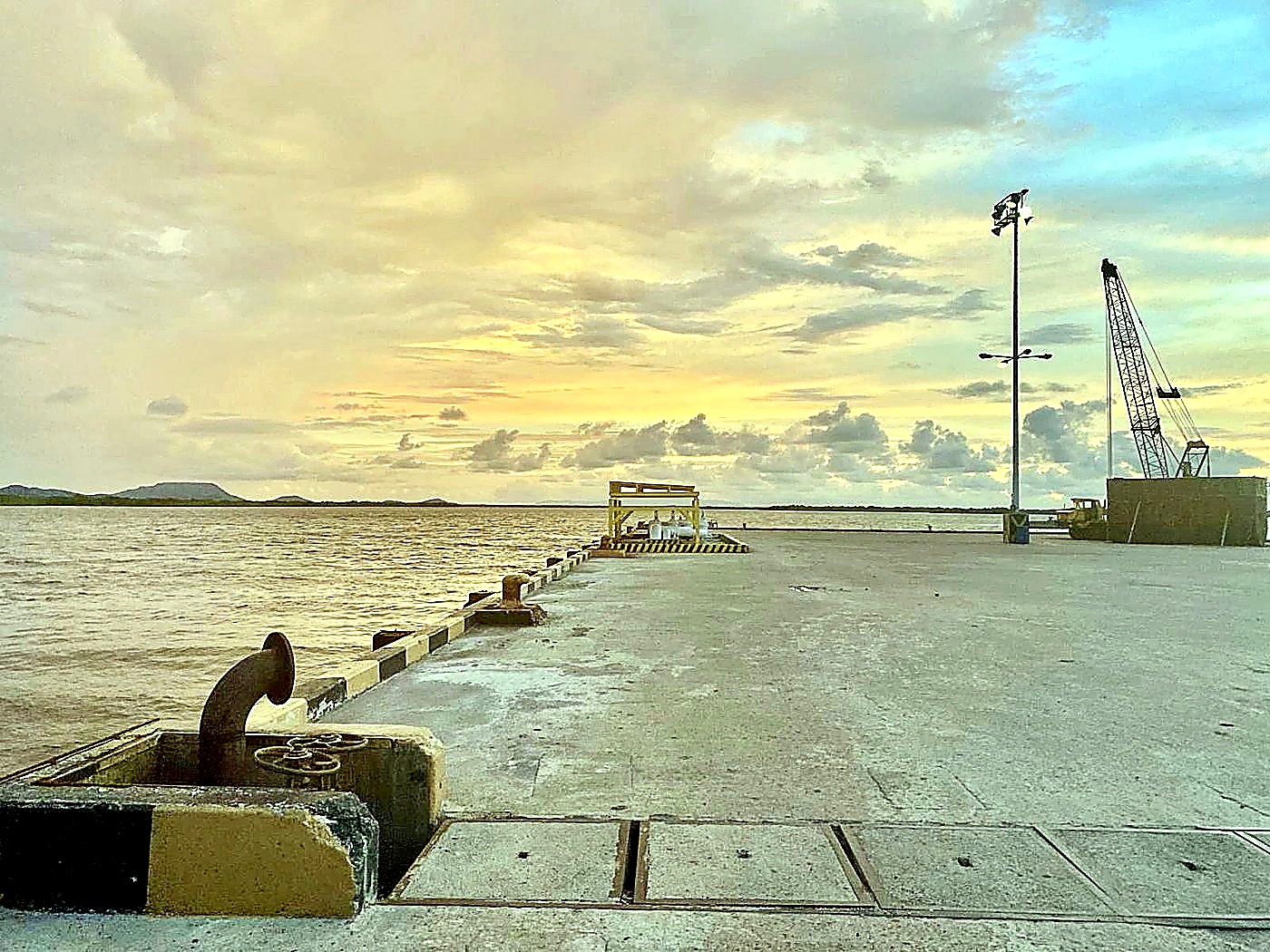 A concrete export dock with loading cranes at sunrise beside calm water at a Central American port
