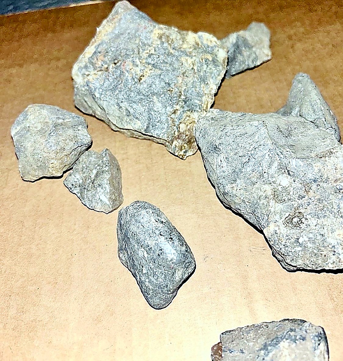 Several grey antimony ore rock fragments of varying size arranged on a tan paper surface for sampling