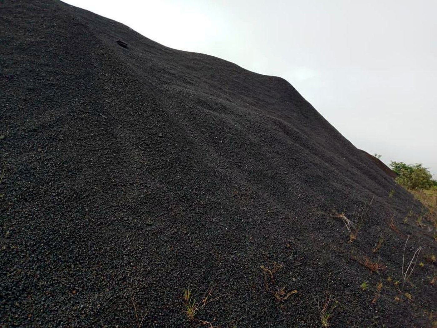 A large sloping stockpile of dark grey-black magnetite iron ore fines under an overcast sky