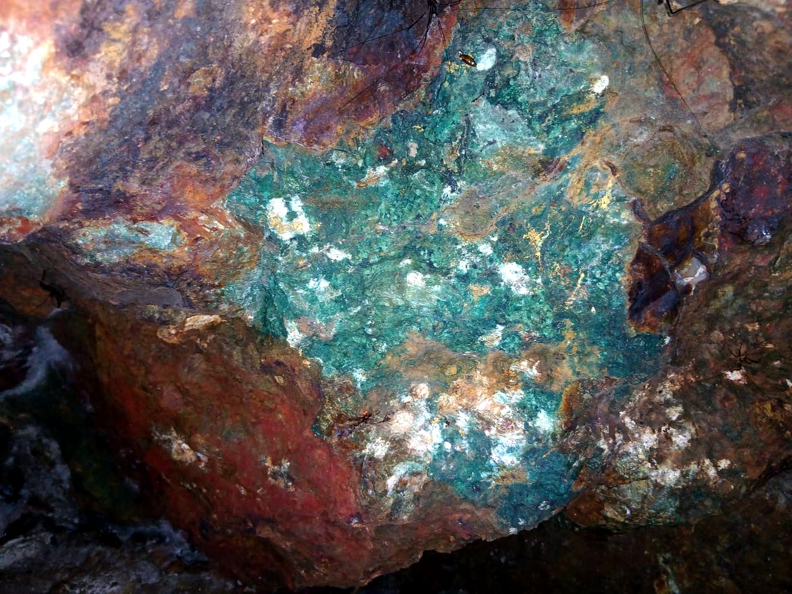 Rock face underground with a large patch of bright green copper carbonate staining surrounded by rust-red oxidised rock
