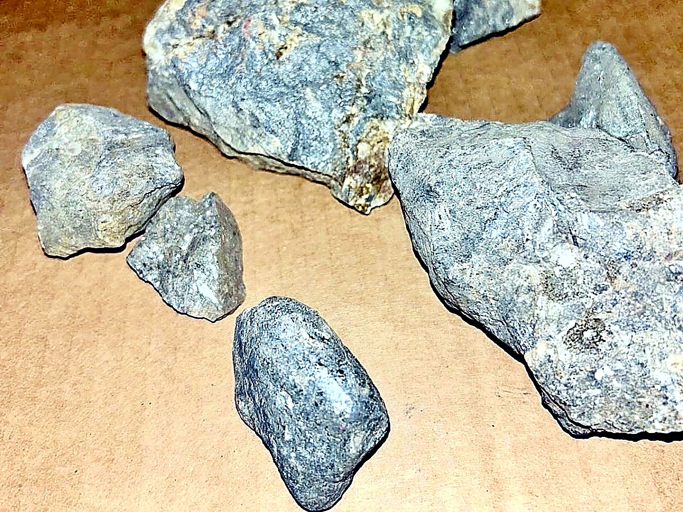 Several grey and tan pieces of quartz-veined host rock laid out for sampling on a brown paper sheet