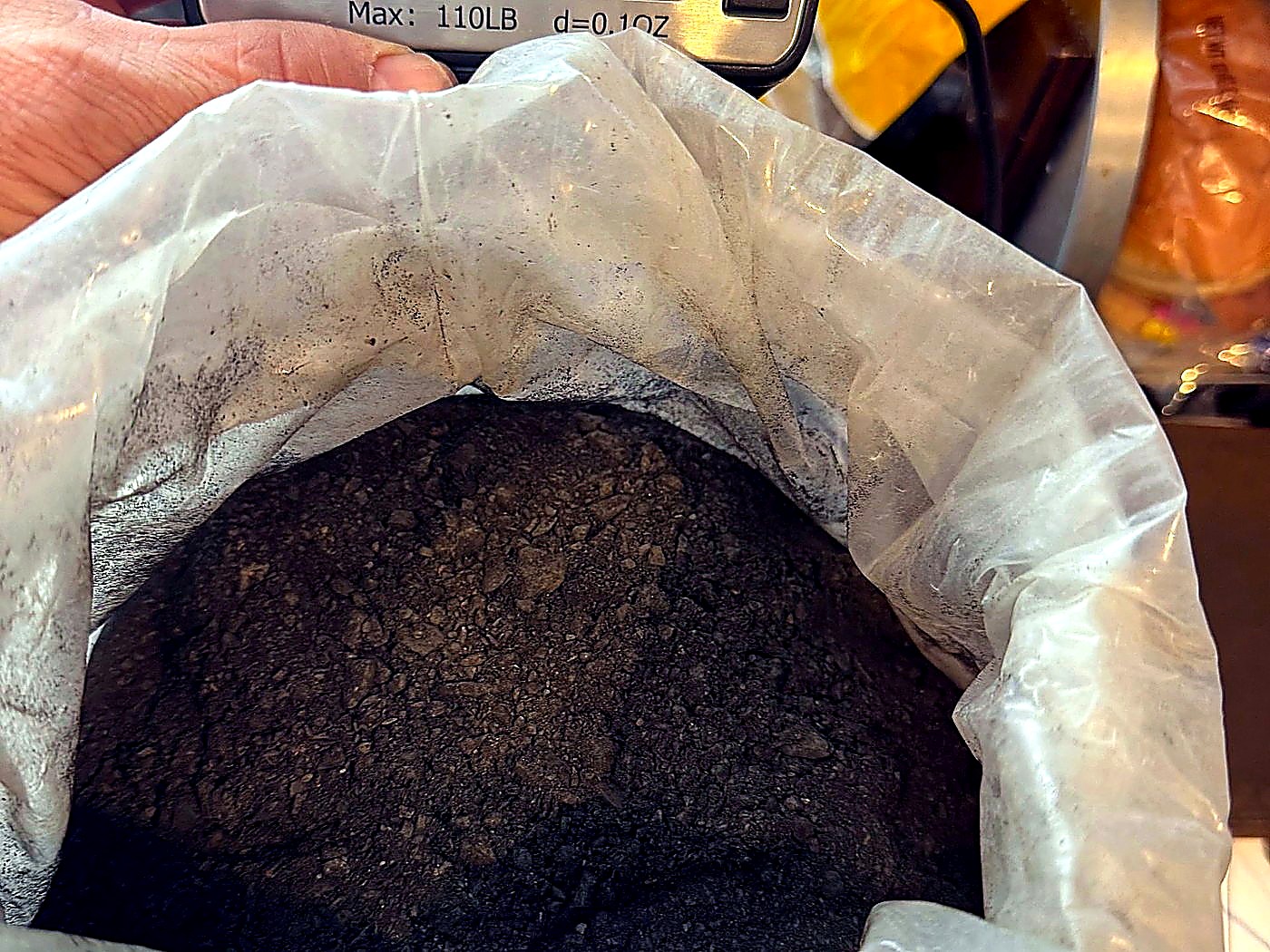 An open woven sack of dark mineral concentrate being weighed and logged at the site weigh station