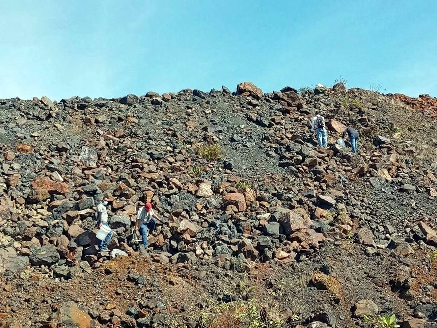 Several locally hired workers walking across a wide rocky quarry surface under a blue sky