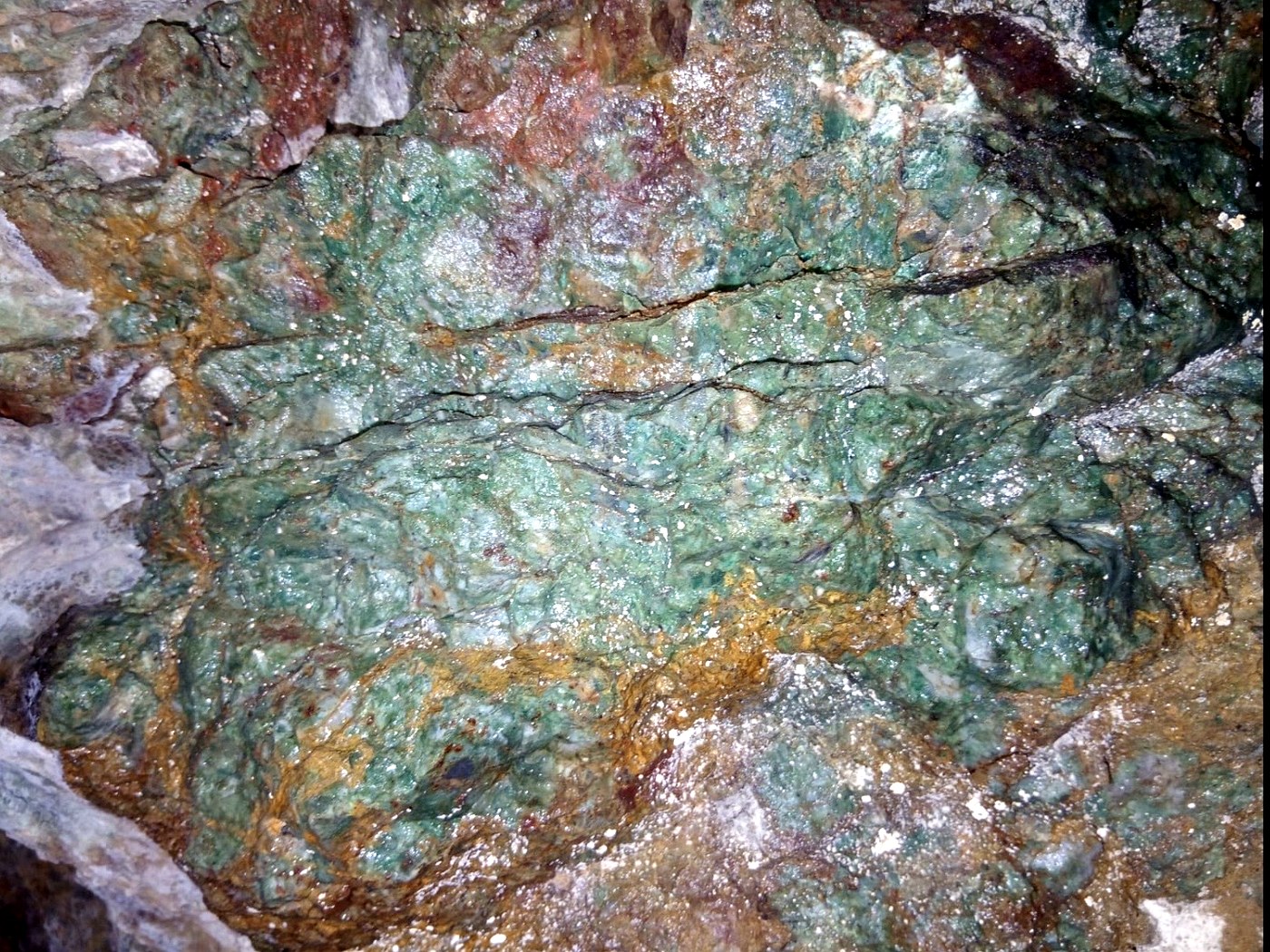 Underground rock face showing a green jade vein surrounded by orange iron oxide and white quartz