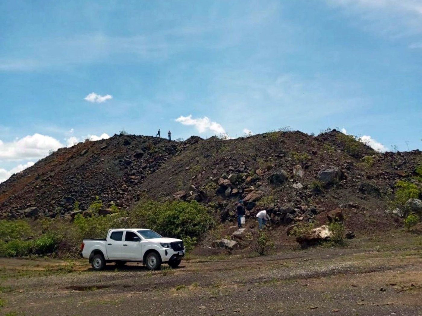 A white pickup truck parked at the base of a dark grey graded ore stockpile on a haulage pad