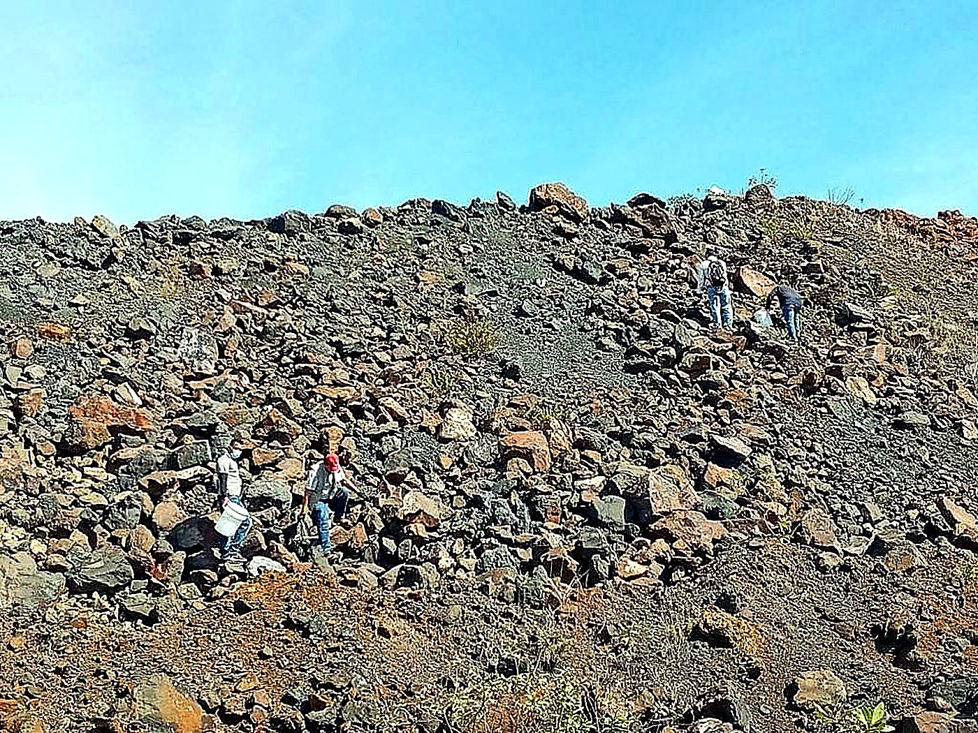 Several locally hired workers walking across a wide rocky quarry surface under a blue sky