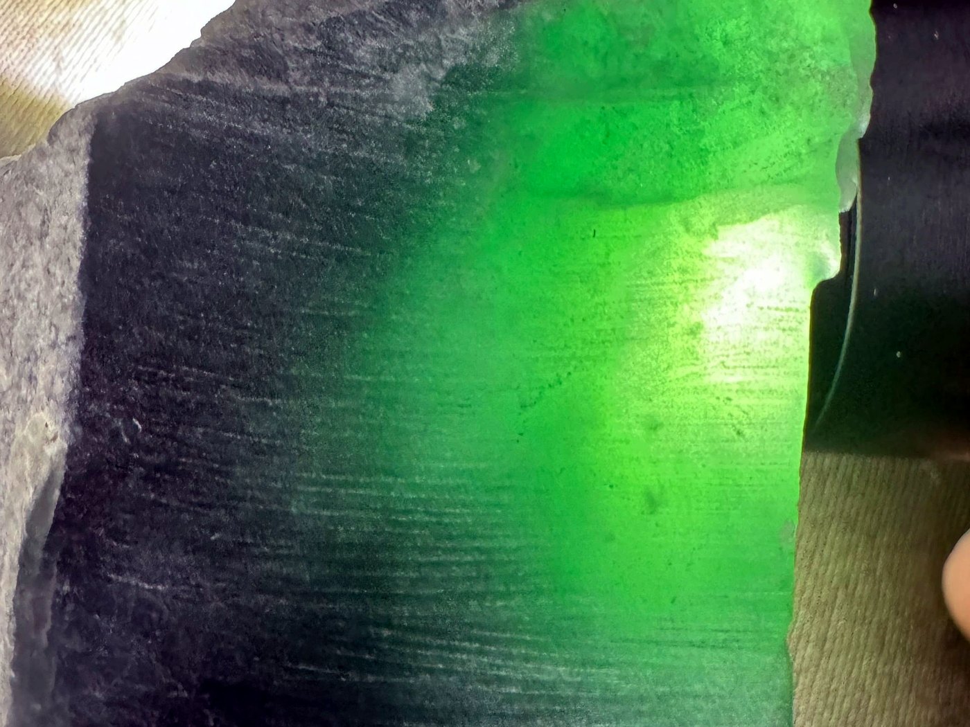 A cut jade slab glowing vivid green as a bright light is shone through it during translucency testing