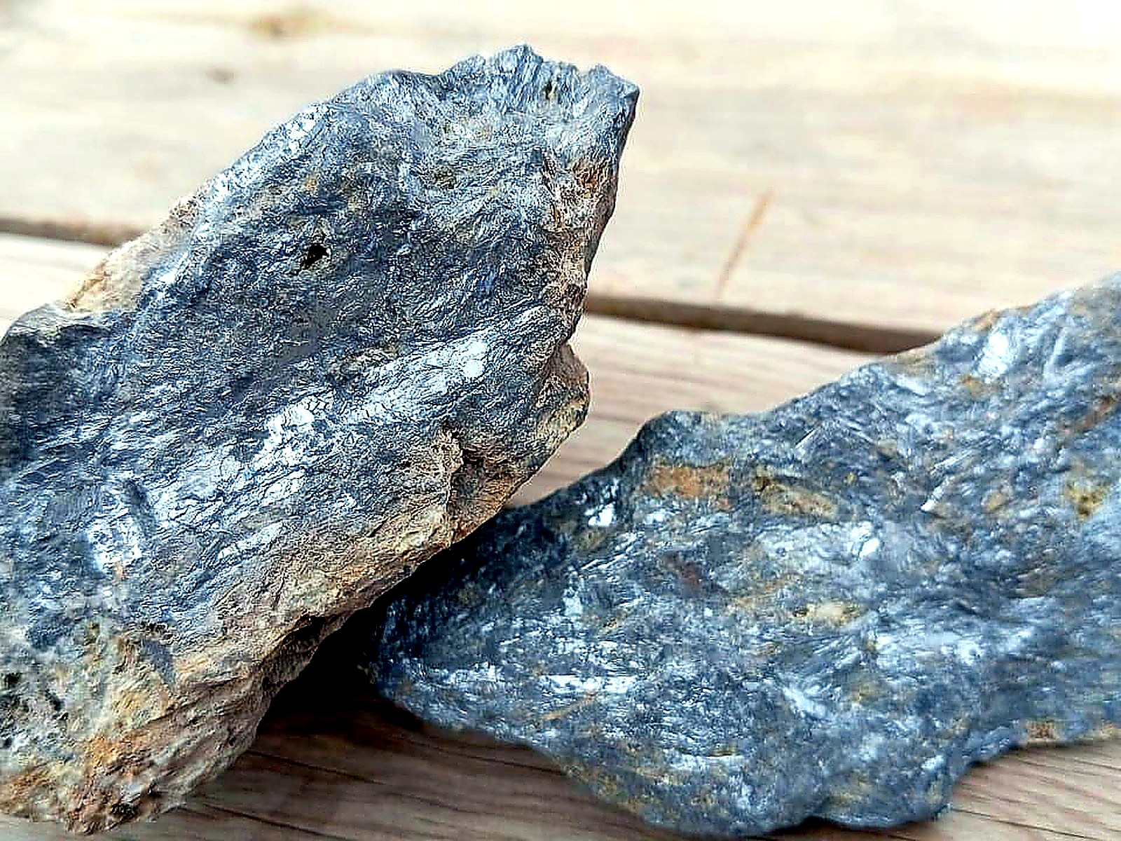 Two metallic silver-grey mineral specimens with bladed crystal texture resting on weathered timber boards