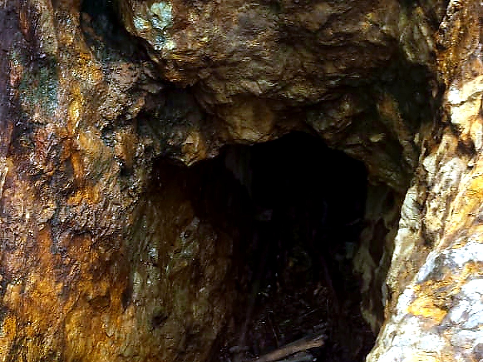 Dark tunnel mouth in yellow-stained quartz rock with rough timber props laid across the entrance