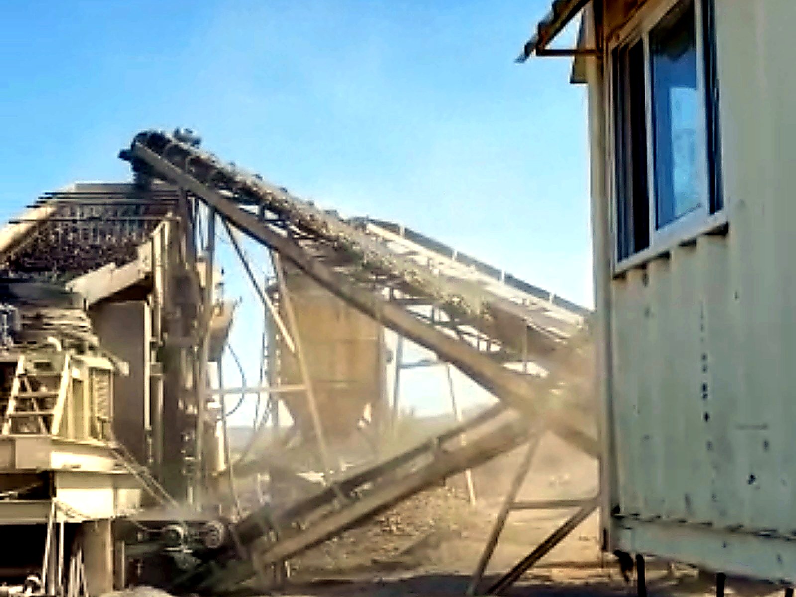 Mine processing yard with screening equipment, crossed conveyors, workshop tools and a white site office