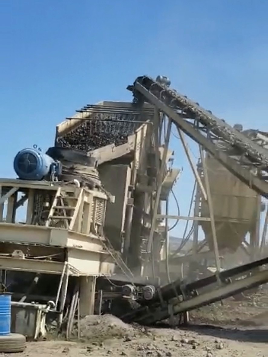 Industrial crushing and screening plant with multiple conveyors operating in a dusty outdoor yard