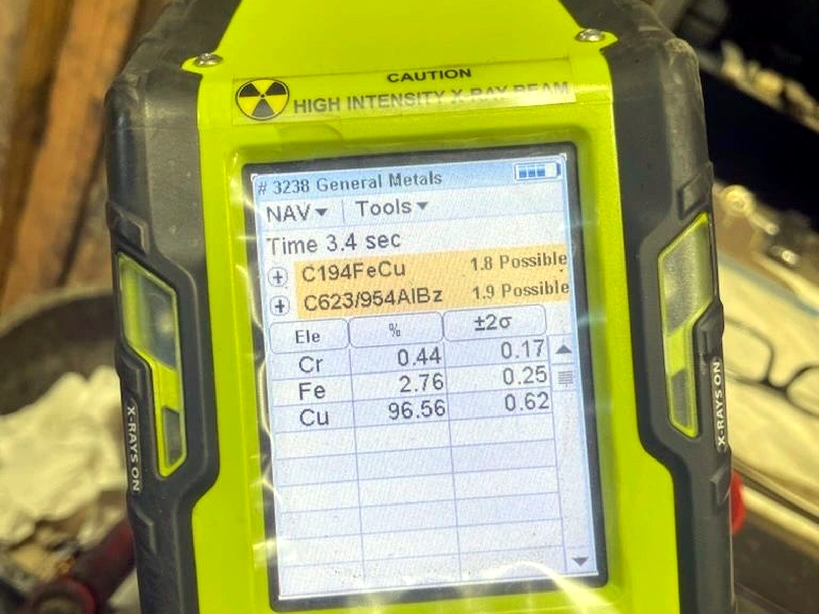 A yellow handheld XRF analyser screen showing a copper reading of 96.56 percent with iron and chromium values