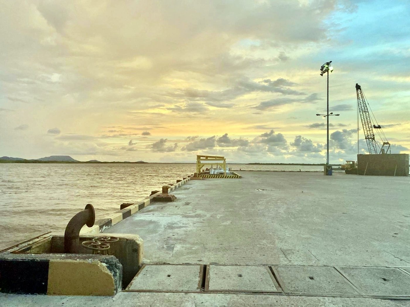 A concrete export dock with loading cranes at sunrise beside calm water at a Central American port