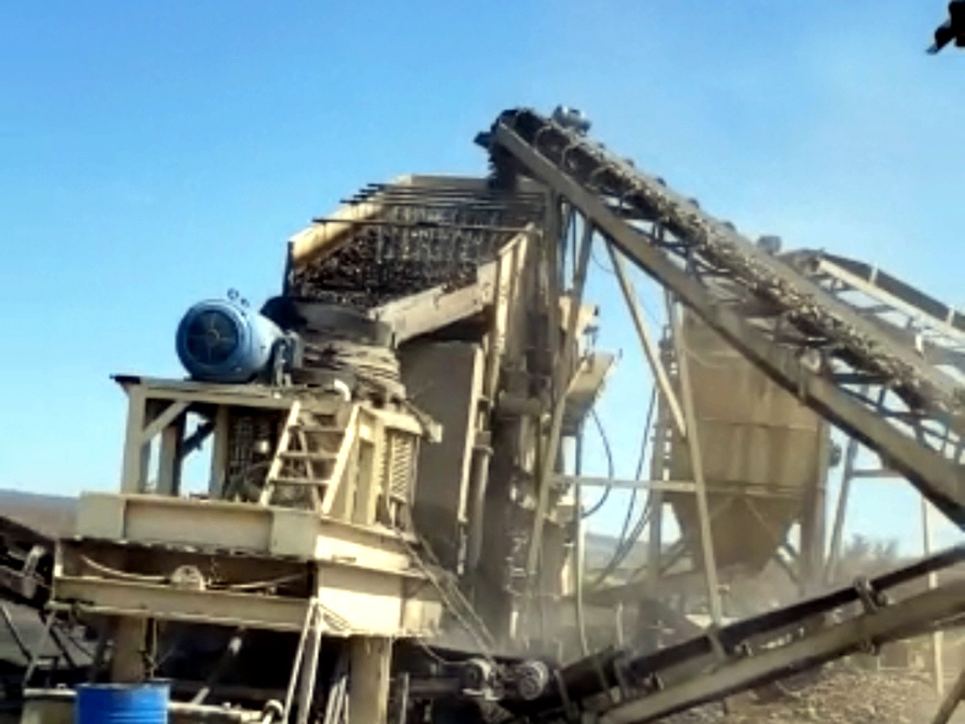 A mobile cone crushing and screening plant with conveyors running under a clear blue sky at a mine site