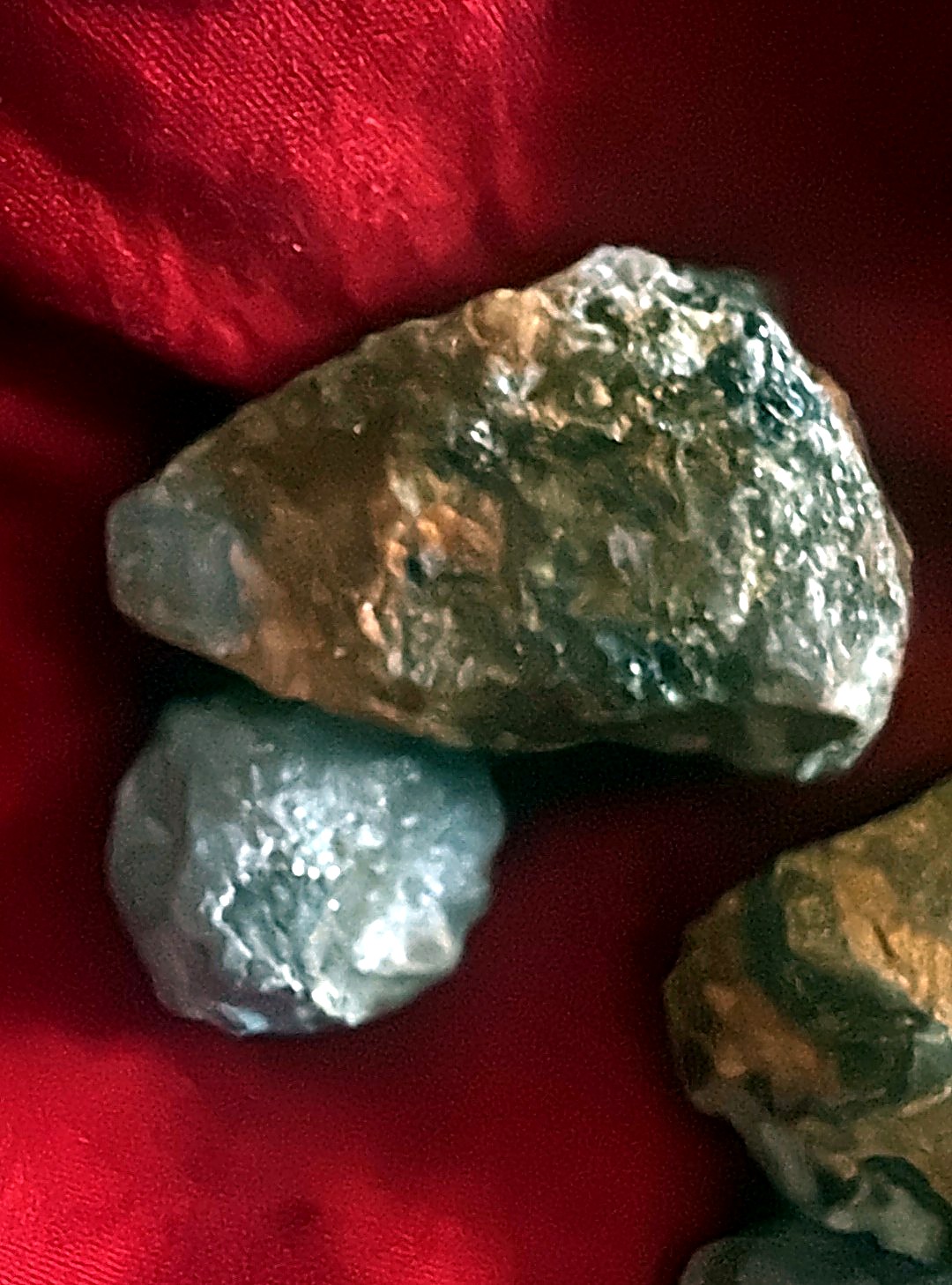 Close-up of a rough ruby corundum stone with translucent red zones beside a smaller grey pebble on red cloth
