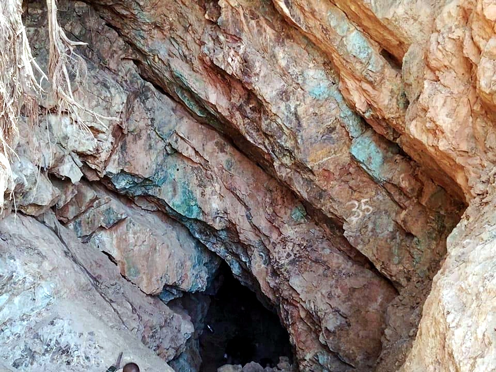 A dark underground adit portal cut into rock covered in turquoise copper oxidation staining