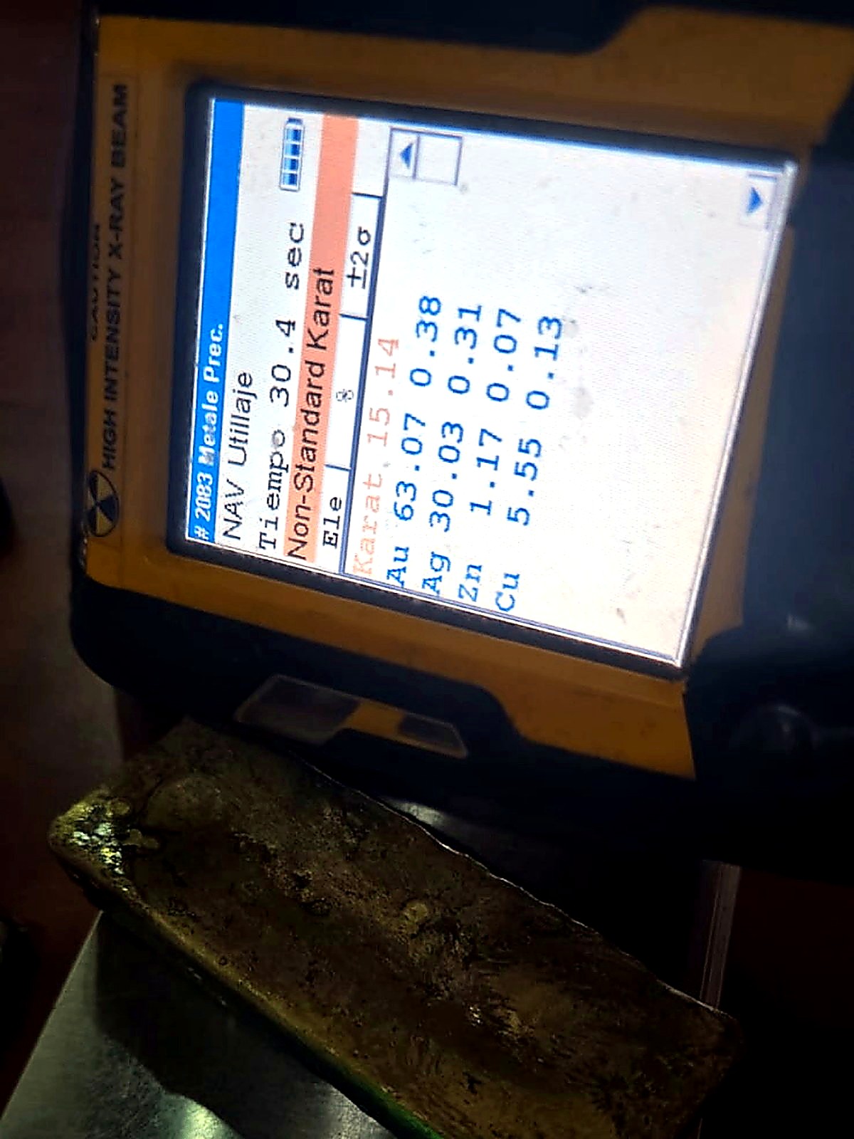 Rectangular gold-silver doré bar photographed beside an XRF analyser screen showing gold and silver percentages