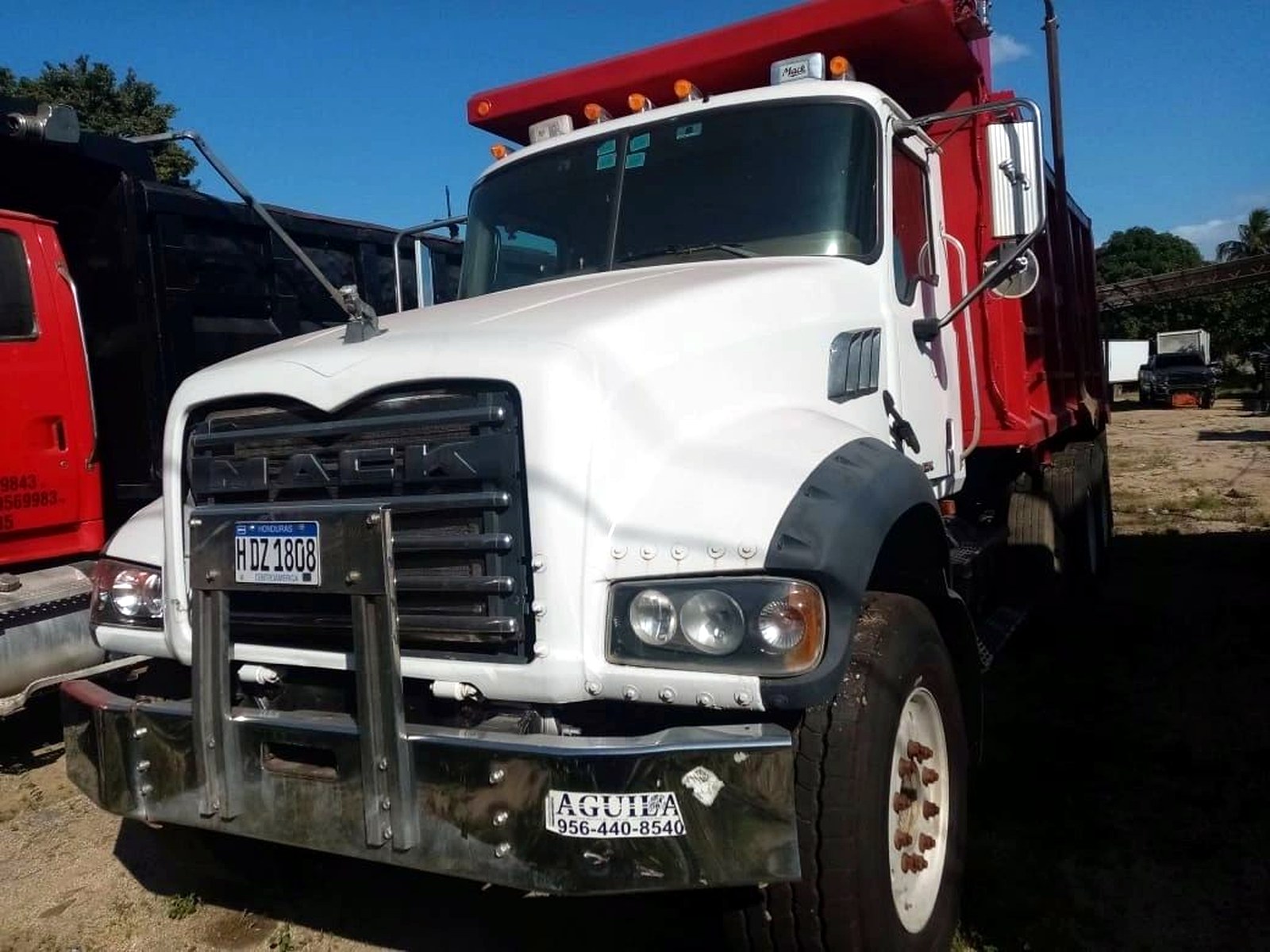 A white and red tipper haul truck parked on a dirt yard at a Central American mine site
