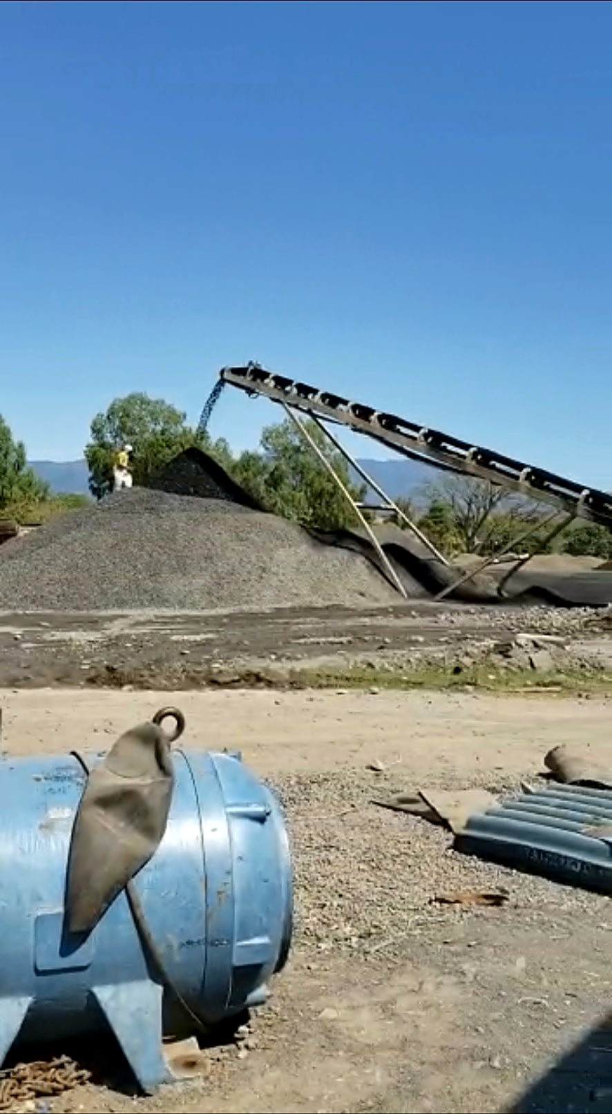 Inclined conveyor discharging crushed grey rock onto a conical outdoor stockpile