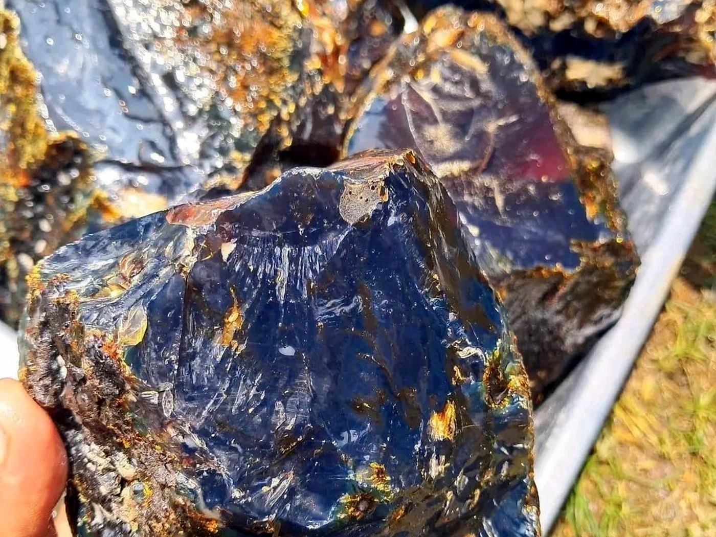 A hand holding a dark glassy sulphide-rich ore block with bright golden mineral inclusions