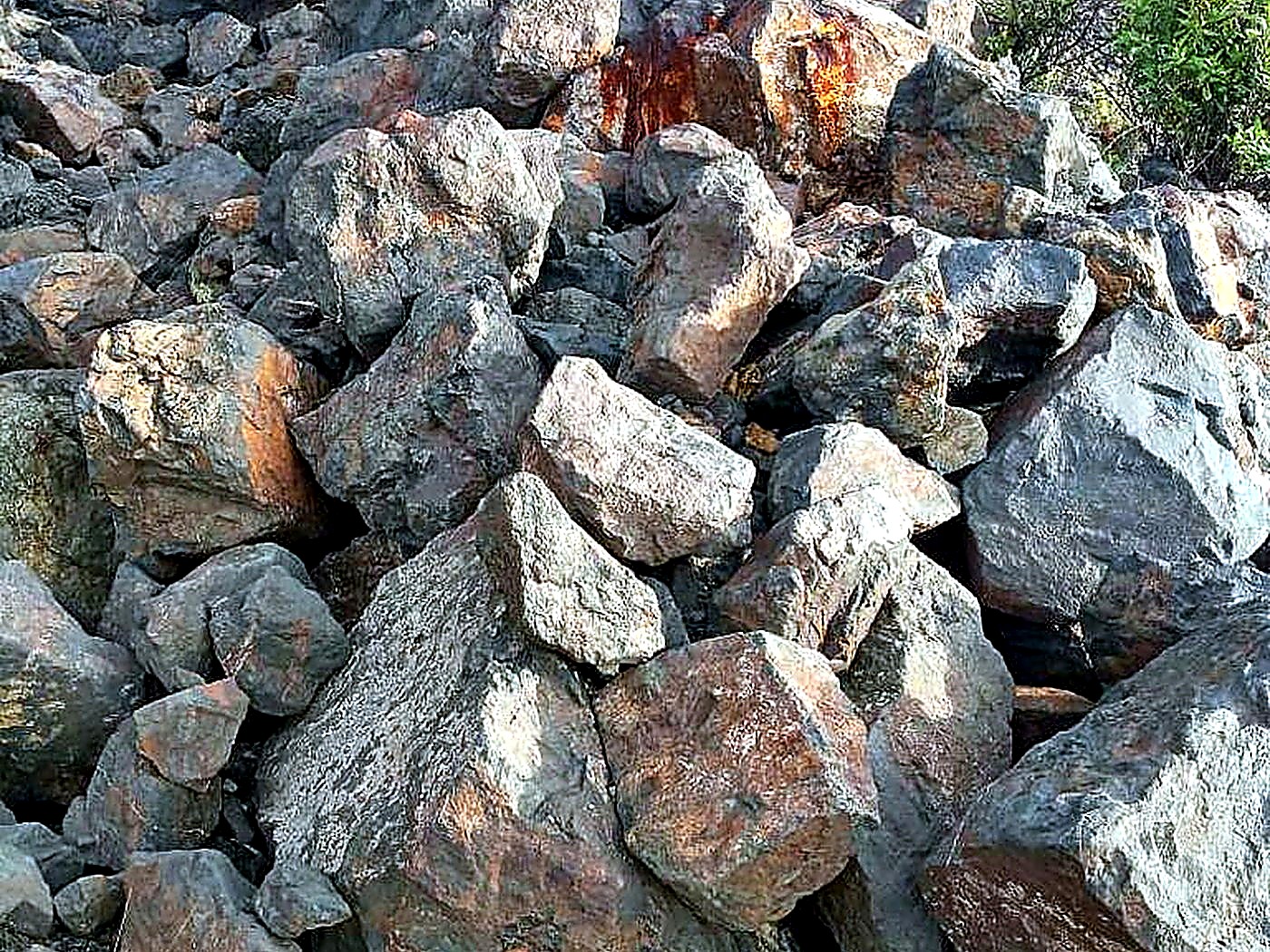 A stockpile of large iron-stained grey and rust-coloured ore boulders on a mine bench